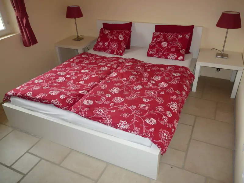 De slaapkamer met een lits-jumeaux, rode dekbedden met bloemen en twee nachtlampjes