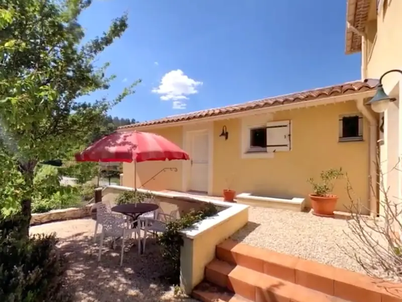 Het terras van het appartement met een rode parasol en een tuintafel met stoelen